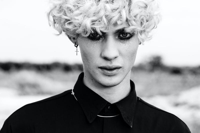 Jeune homme aux yeux maquillés en noir, avec cheveux frisés blonds